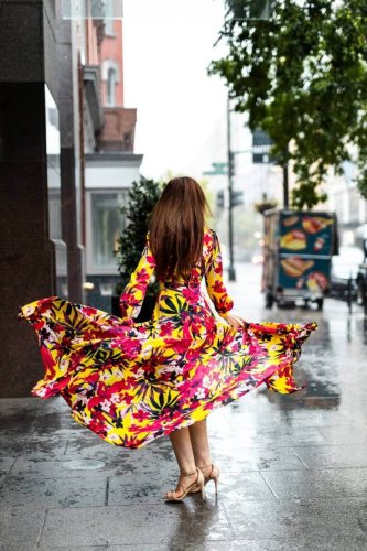 Josilee Adams twirls joyfully in a flowing yellow floral dress on a rainy city sidewalk, the motion of the fabric capturing playful elegance.